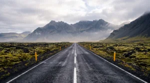 An empty Icelandic road through moss-covered lava, with mountains in the mist