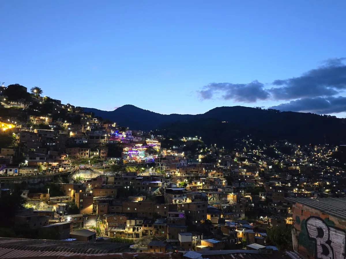 Νυχτερινή άποψη της Comuna 13 στο Μεδεγίν με πολύχρωμα φώτα και σπίτια στους λόφους.