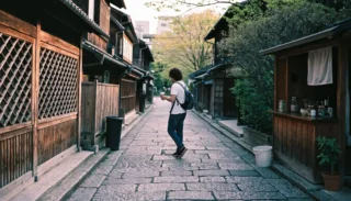 A traveller with a coffee in hand strolling a stone-paved lane lined with wooden houses in Kyoto's old town
