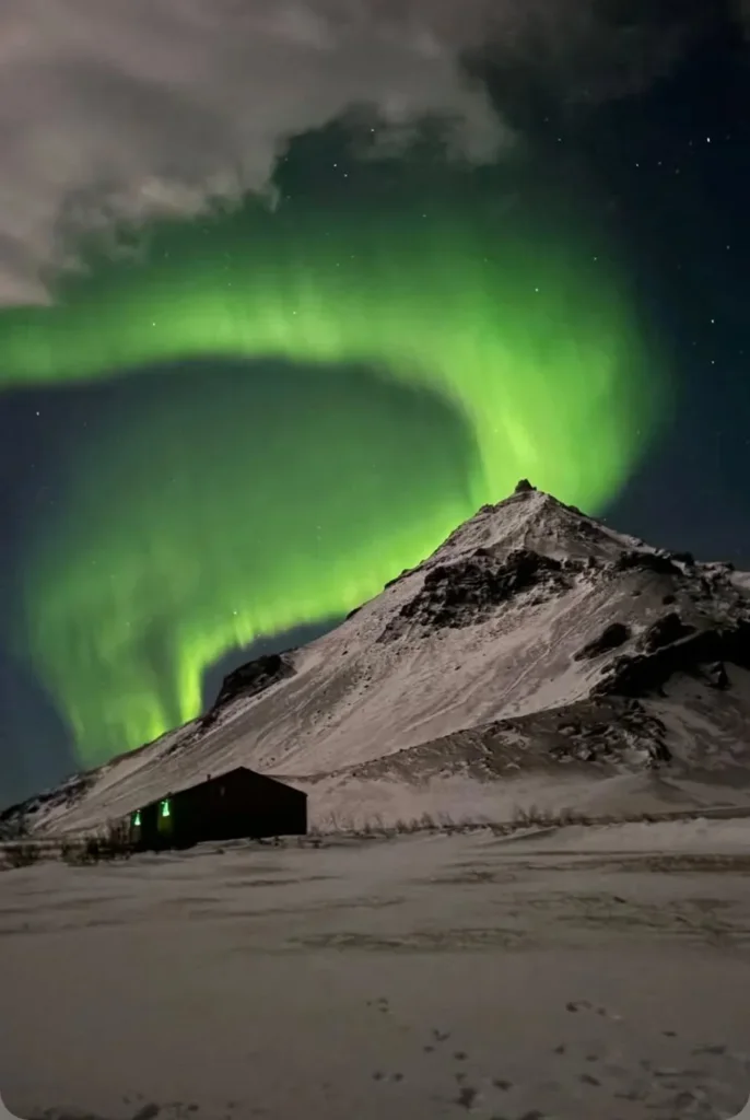 Green aurora over the snowy mountain at Arnarstapi